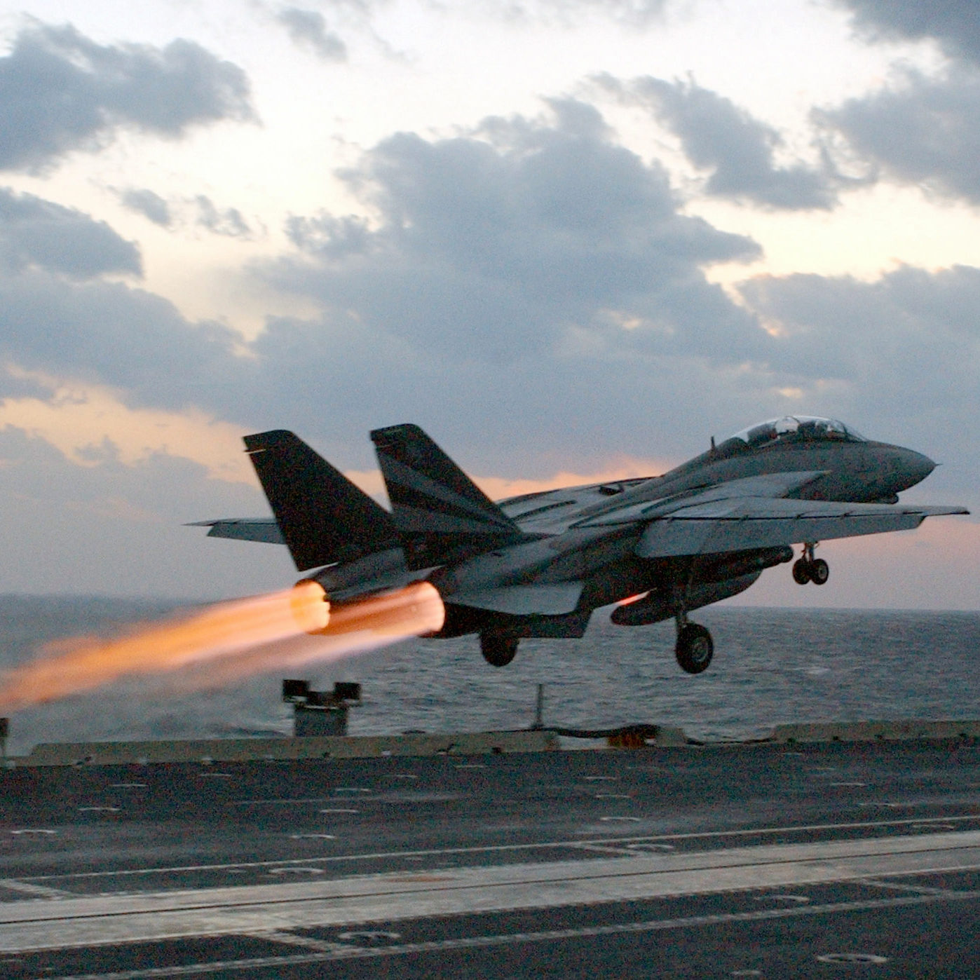 An F-14 launching from an aircraft carrier deck at dusk