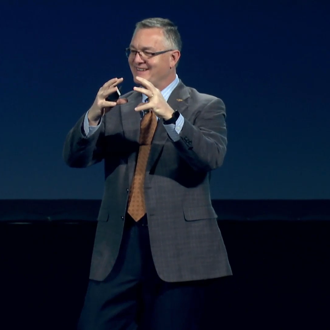 John Ramstead speaking on a dark stage