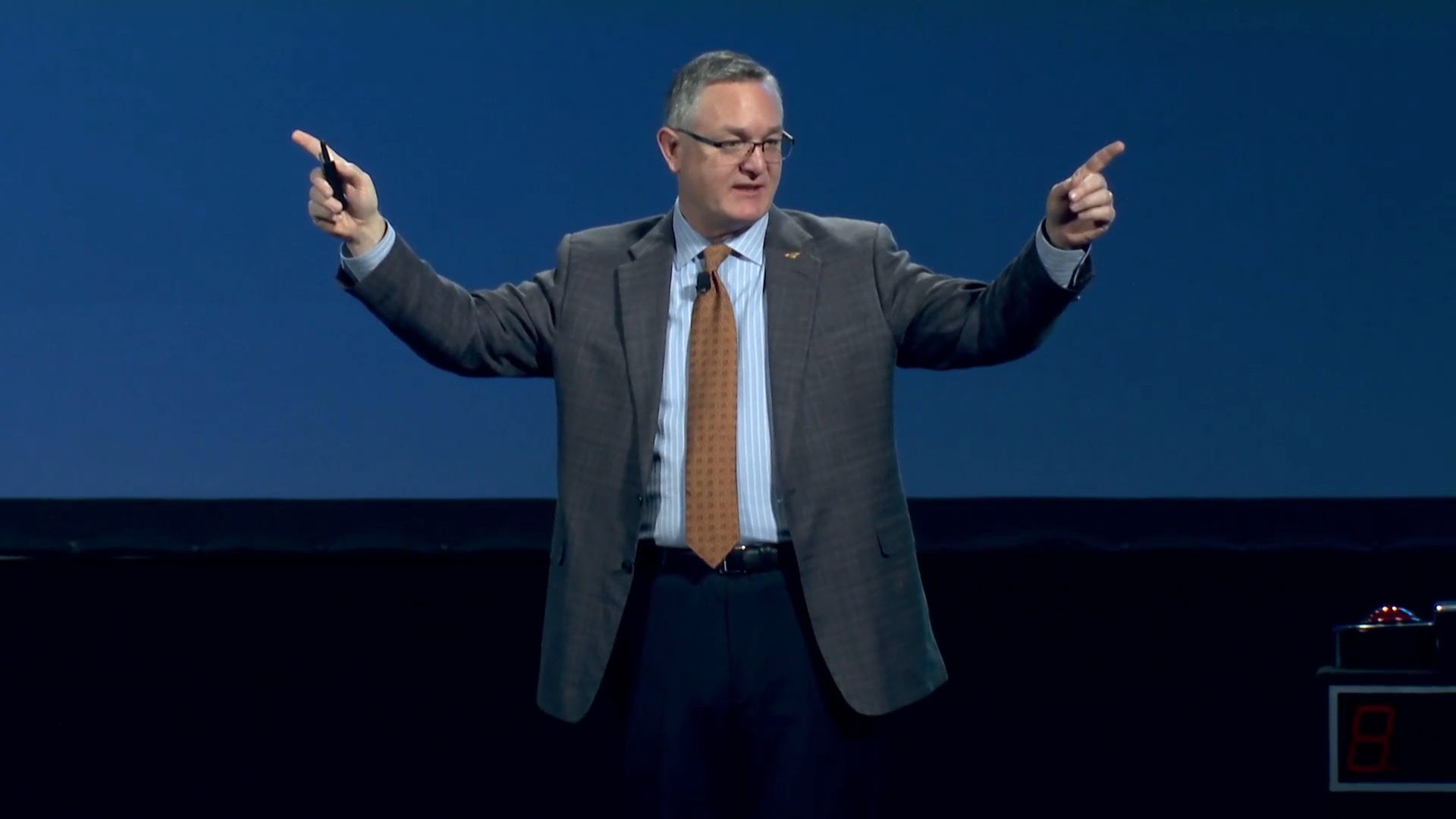 John Ramstead on a dark stage, pointing out to the audience with both hands