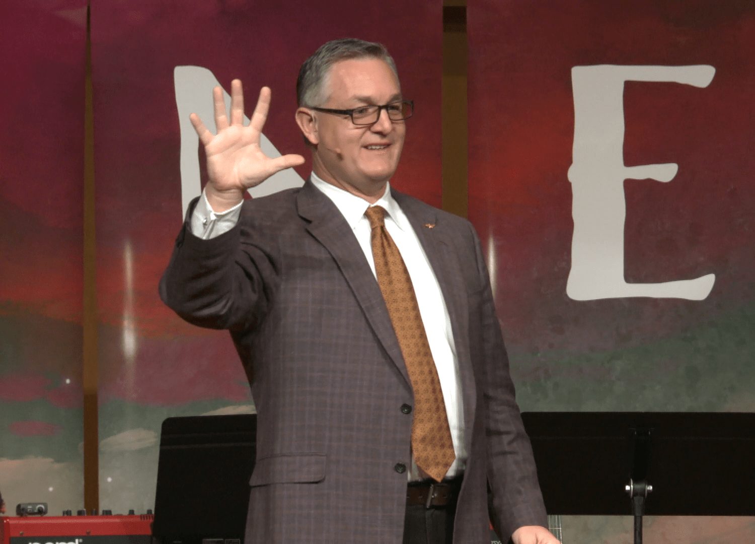 John Ramstead on stage, raising an open hand